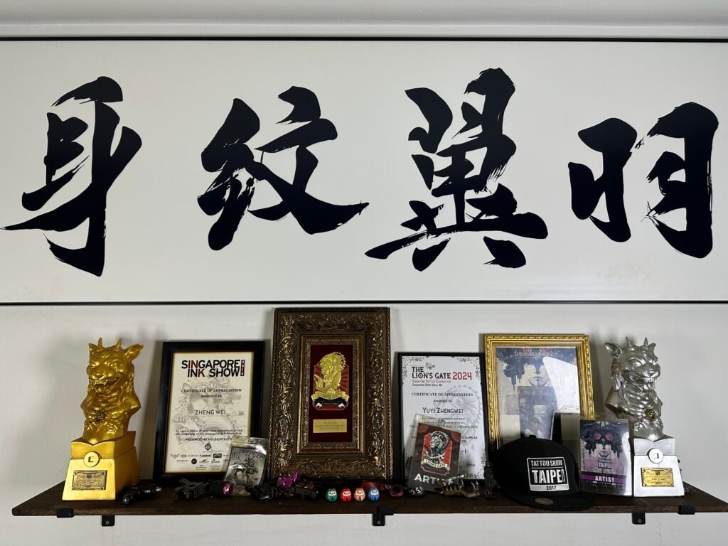 Framed calligraphy, certificates and tattoo convention awards on a studio shelf