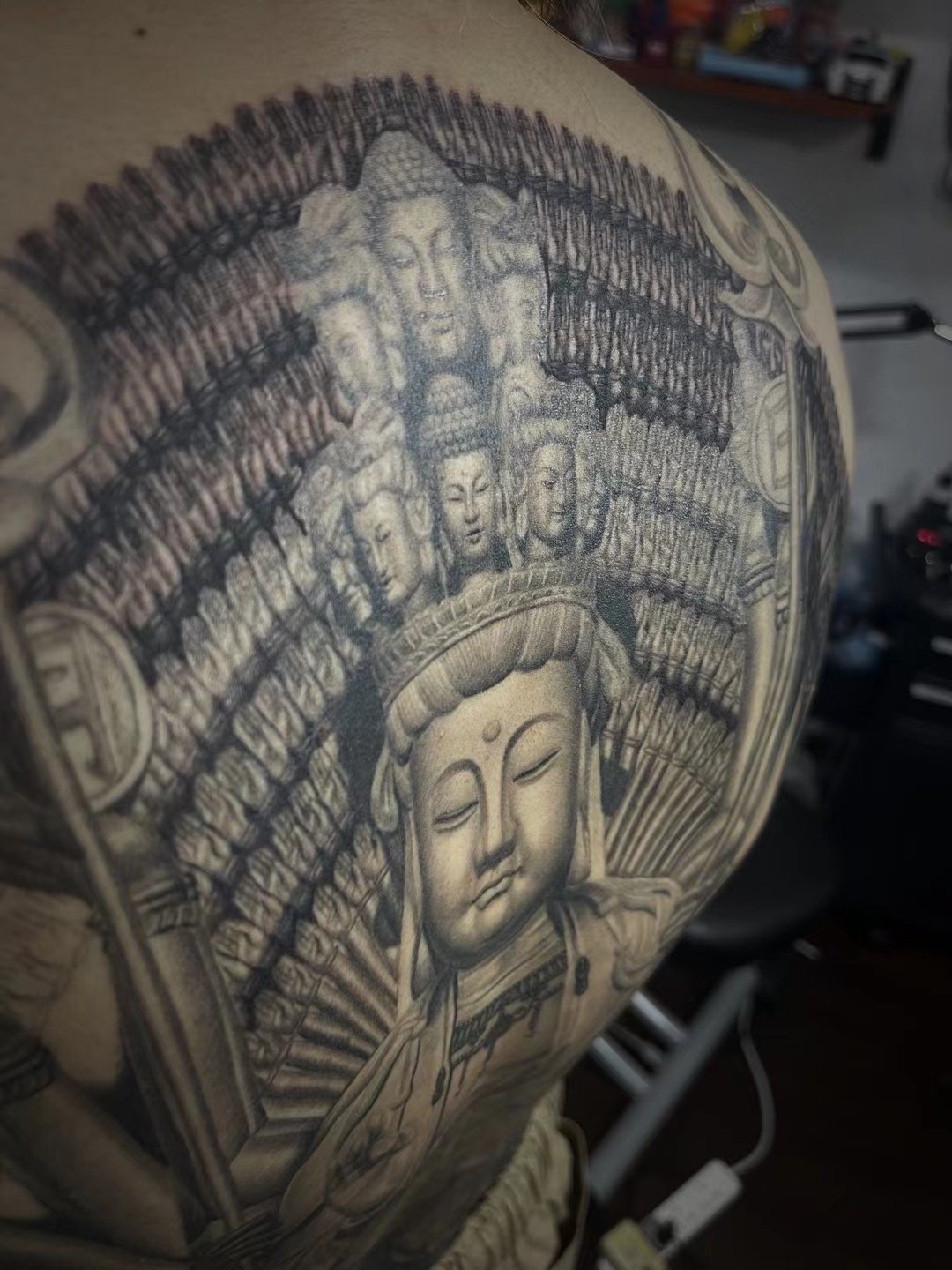 Close view of the central Guanyin figure and repeated hands in a black-and-grey back tattoo