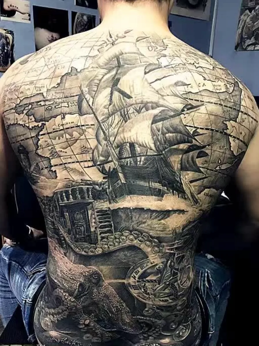 Black-and-grey ship and map tattoo covering a person’s back