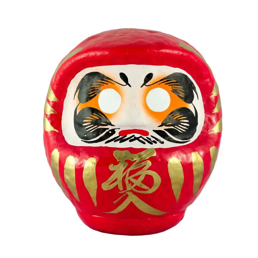 Red Daruma doll with white unpainted eyes, black facial details and gold decoration