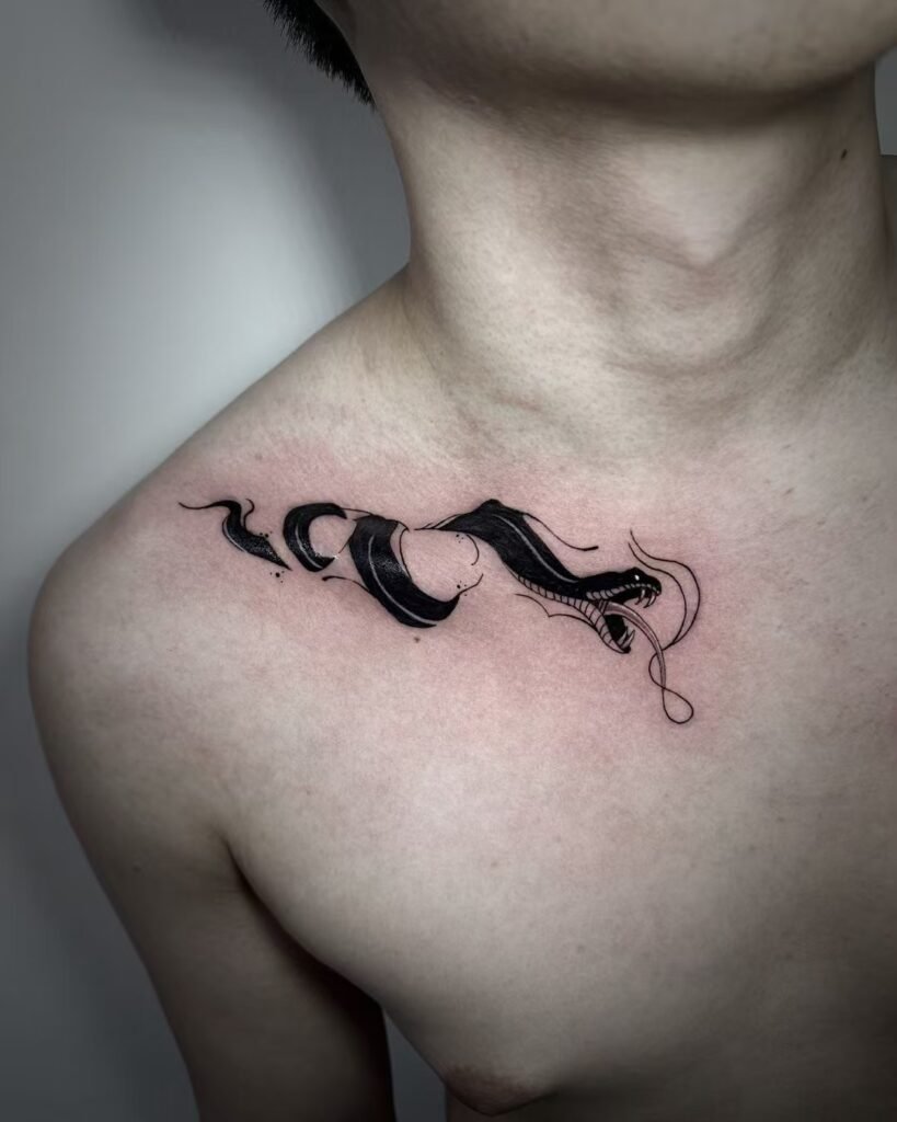 Black flowing serpent-like ornament tattoo across the collarbone