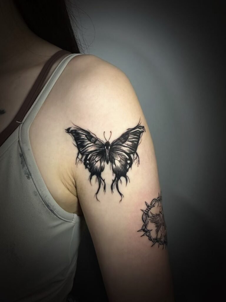 Black butterfly tattoo with pointed wing details on the upper arm