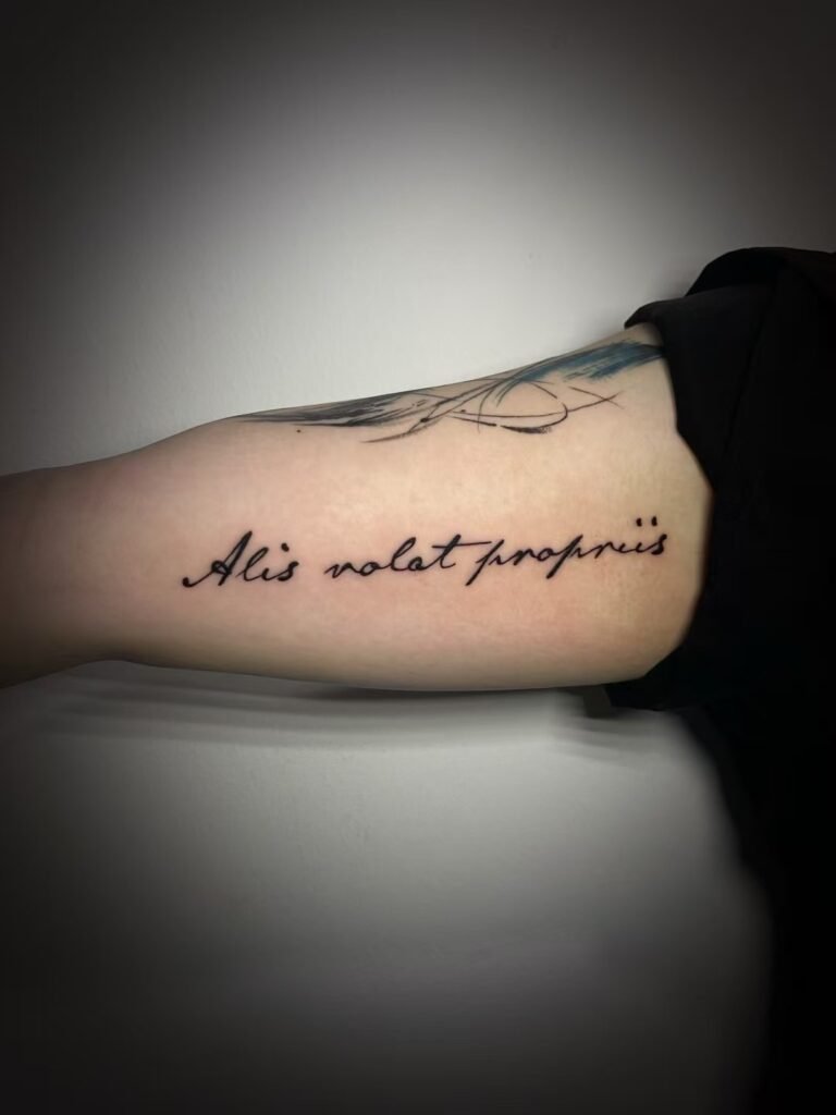 Horizontal cursive lettering tattoo along the inner upper arm