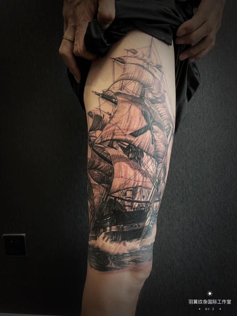 Black-and-grey sailing ship tattoo along the thigh